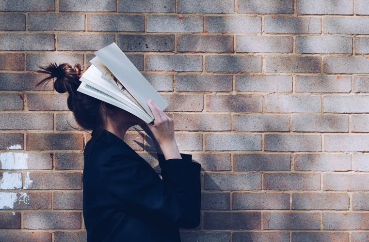 Frau hält sich ein Buch vor das Gesicht. Foto: Unsplash
