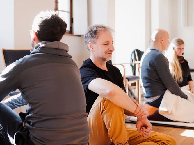 zwei Männer sitzen diagonal gegeüber mit geschlossen Augen