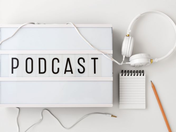 weißes Schild mit schwarzem Schriftzug Podcast und einem Kopfhörer daneben