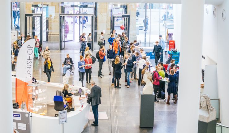 Farbfoto: Blick von der Balustrade in das Neue Augusteum zum Tag der Lehre hinein. Einige Menschen stehen an Informationsständen und unterhalten sich.