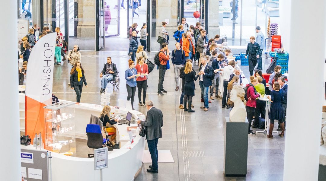 Farbfoto: Blick ins Augusteum der Universität Leipzig, einige Menschen stehen an Ständen und unterhalten sich