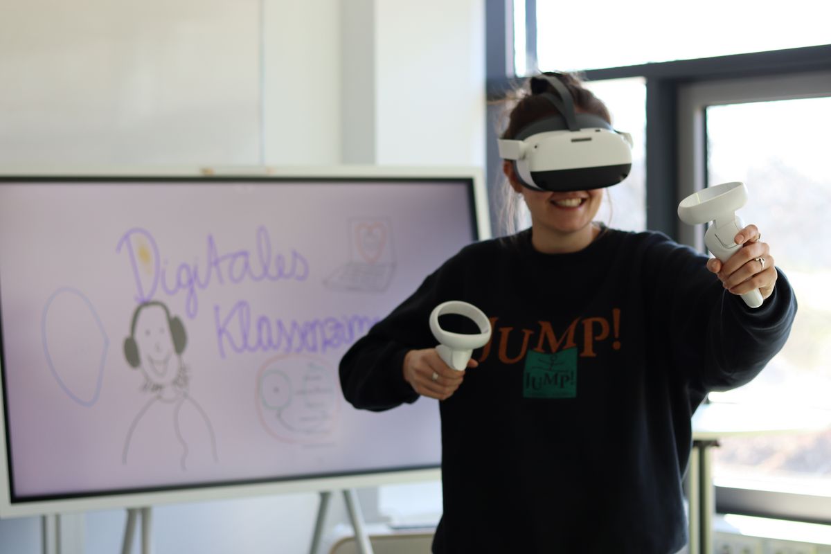 zur Vergrößerungsansicht des Bildes: Das Foto zeigt eine junge Frau mit einer VR-Brille, die vor einer beschrifteten interaktiven Tafel steht. Sie hat sichtlich Freude am Ausprobieren.