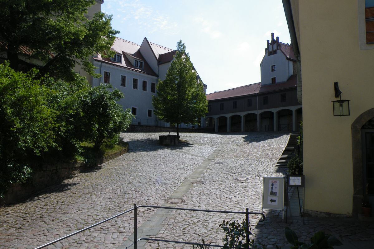 zur Vergrößerungsansicht des Bildes: Zu sehne ist der Innenhof eines Klosters mit einem grünen Baum in der Mitte. 