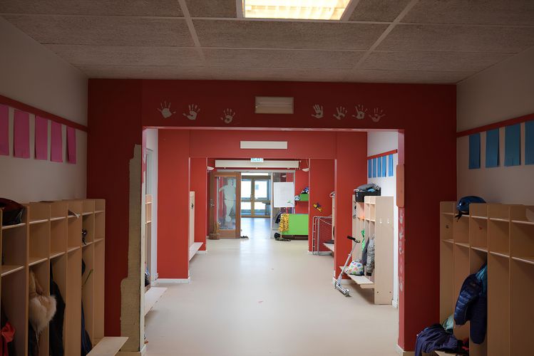 Das Bild zeigt den Gang einer Schule mit Garderoben und farbigen Wänden.