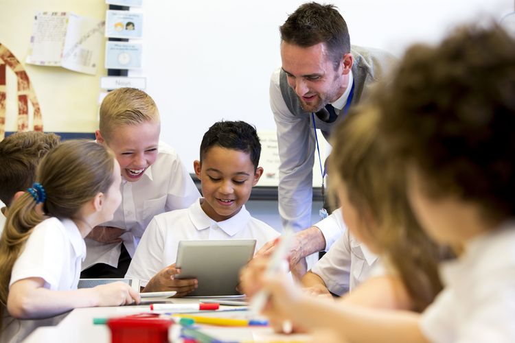 Ein männlicher Lehrer beaufsichtigt eine Gruppe von Schülern, die an digitalen Tablets arbeiten.
