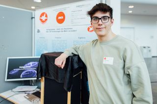 Das Foto zeigt eine junge Person, die im Rahmen des Jungend forscht Wettbewerbs vor einem Projektstand posiert. 