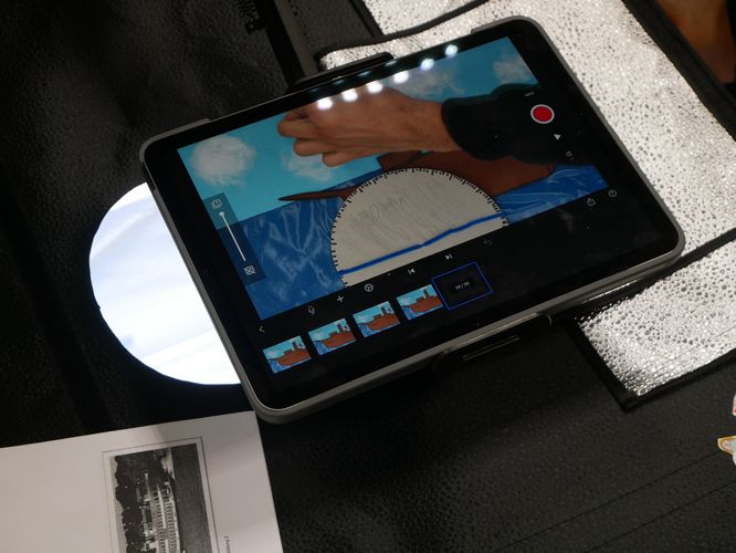 Ein von oben fotografiertes Tablet auf dem die App "Stop-Motion Studio" geöffnet ist. Eine Hand bewegt im Bild ein Bildelement. 