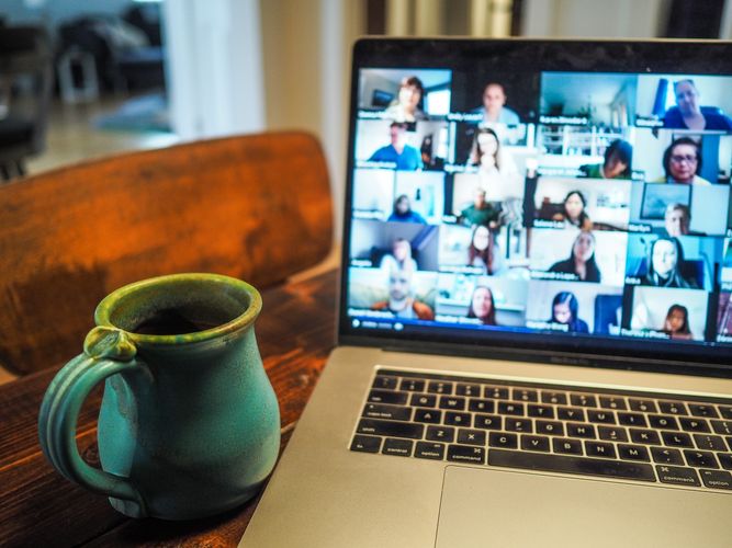 Es ist ein laptop mit einer Zoom Konferenz zu sehen. Daneben steht eine grüne Tasse mit Tee. 