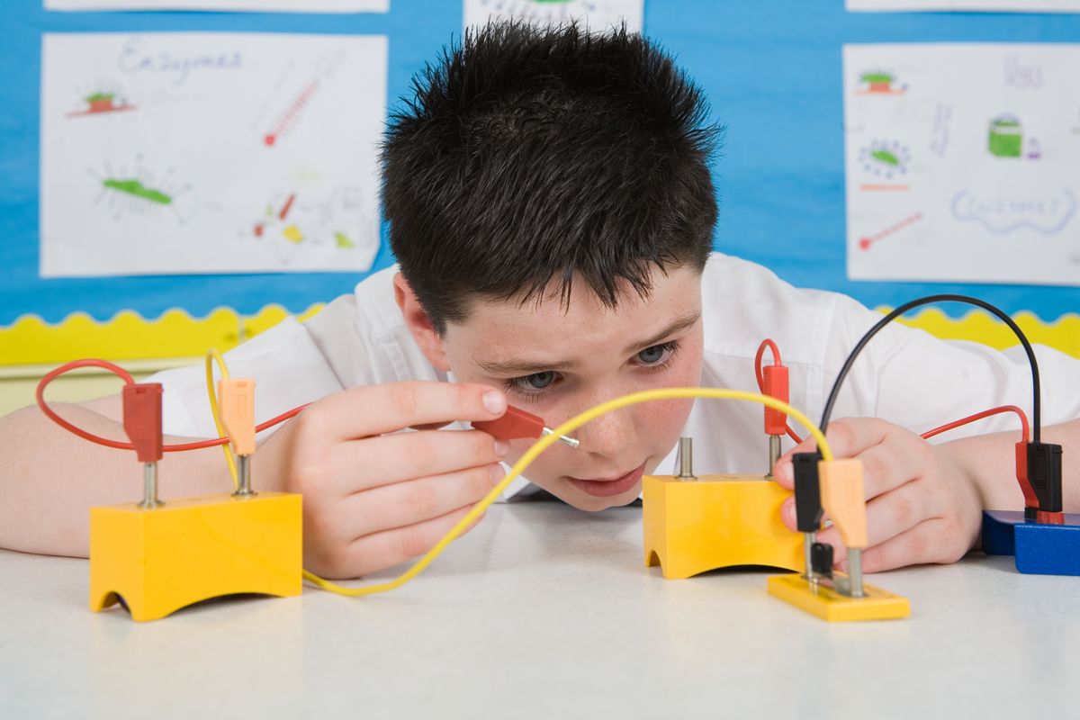 Auf dem Foto ist ein circa 11 jähriger Junge im Physikunterricht abgebildet. Er hat einen selbst gebauten Schaltkreis vor sich auf dem Tisch stehen und probiert sehr konzentriert die elektrische Ladung aus.