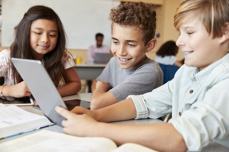 drei Kinder sitzen an einem Tisch und schauen gemeinsam auf ein Blatt, welches eines der Kinder in der Hand hält.