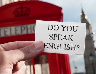 Auf diesem Foto hält eine Hand einen Zettel in die Bildmitte mit dem Text: Do you speak English? Im Hintergrund sieht man eine typische Britische rote Telefonzelle und den Bigben.